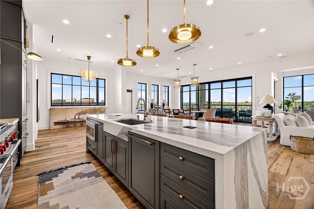 Open-concept kitchen and living area with outdoor connection. This open-concept layout seamlessly connects kitchen, living, and outdoor zones for effortless flow. A central island anchors the space, while large windows and glass doors extend the living experience beyond the interior. Designed for luxurious entertaining and relaxed sophistication.