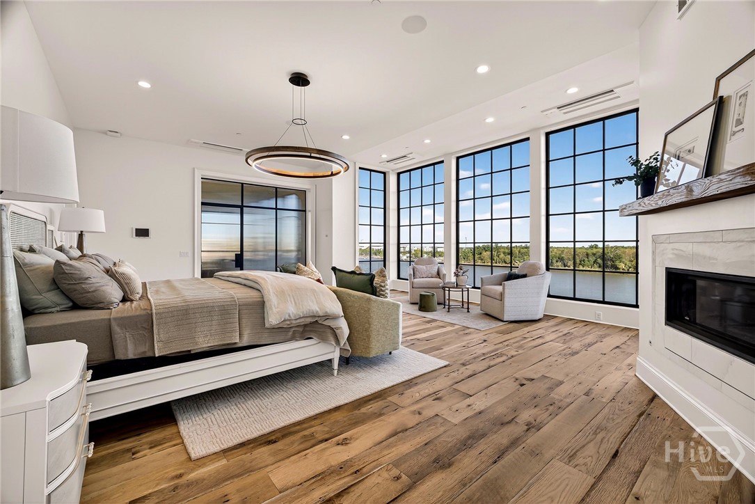 Primary Suite with lake view and floor-to-ceiling windows. A dramatic wall of glass frames sweeping lake views, creating a tranquil focal point in this expansive bedroom suite. The layout includes a cozy sitting area and integrated fireplace, offering both visual balance and functional luxury. An exceptional retreat designed for serenity and sophistication.