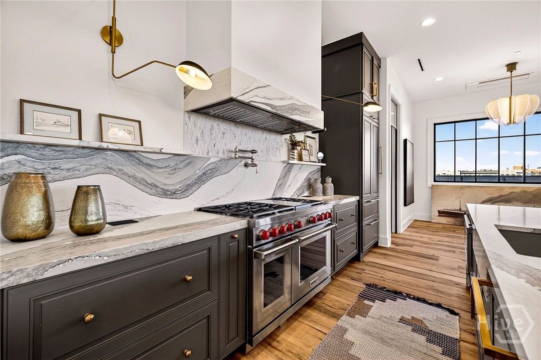 Kitchen with dramatic marble and large window. A bold, gallery-style kitchen layout centers around dramatic marble surfaces and professional-grade appliances. The expansive window floods the space with natural light, enhancing the clean lines and vertical symmetry. Ideal for elevated culinary experiences and visual impact.
