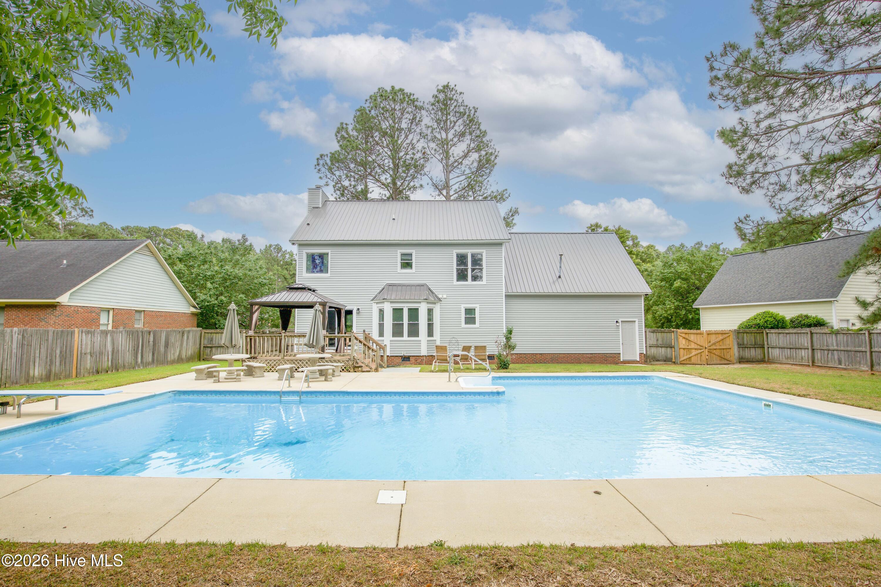 Wide-angle view of the backyard retreat highlighting the large in-ground swimming pool, expansive patio space, mature trees, and rear exterior of the home. This setup offers exceptional outdoor living potential with room for gatherings, cookouts, poolside seating, and recreation. Homes with pools and no HOA restrictions continue to generate strong buyer interest throughout the Fayetteville and Fort Bragg real estate market.
