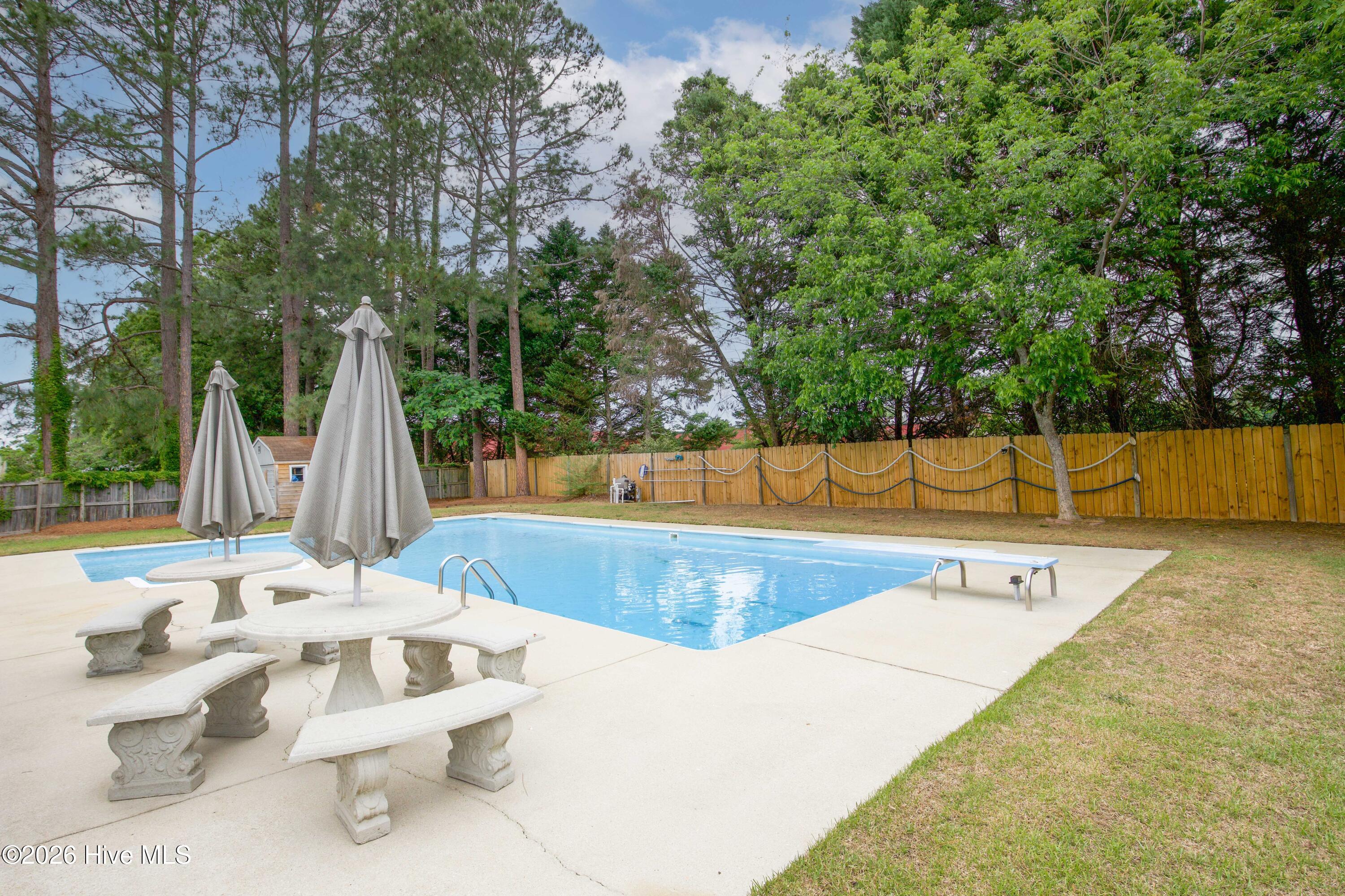 Outdoor dining and seating area positioned alongside the pool provides additional space for entertaining, relaxing, and enjoying the backyard retreat. The spacious fenced yard and mature trees create a comfortable outdoor environment designed for gatherings, cookouts, pool parties, or peaceful evenings at home. No HOA restrictions offer added flexibility rarely found in similar Fayetteville properties.
