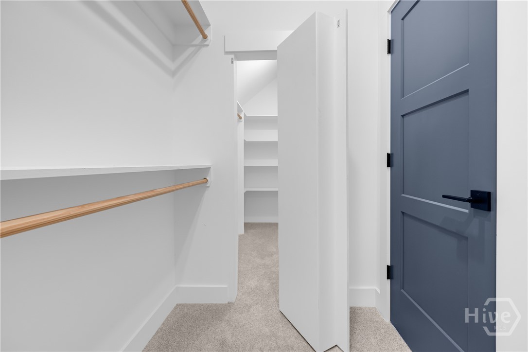 Secret Passageway in Walk-in closet featuring light-colored carpeting, multiple shelving units, and two wooden hanging rods