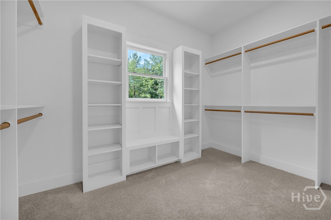 Walk-in closet featuring built-in shelving, hanging rods, an integrated window bench, and light gray carpet