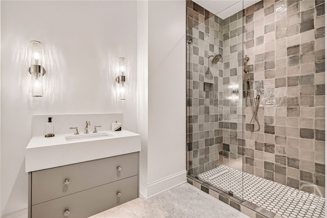 Bedroom 3 Ensuite - The ensuite bath features a clean, modern layout with a floating vanity and integrated sink, framed by ambient lighting. A glass-enclosed walk-in shower with mixed tile textures adds depth and sophistication. Designed for streamlined functionality and spa-like comfort.