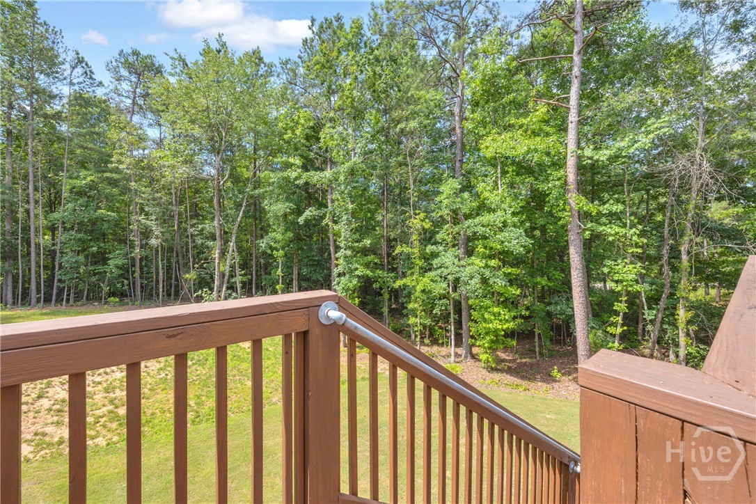 Wood-toned deck railing with a metal handrail overlooking a sloped grassy area and extensive tree line