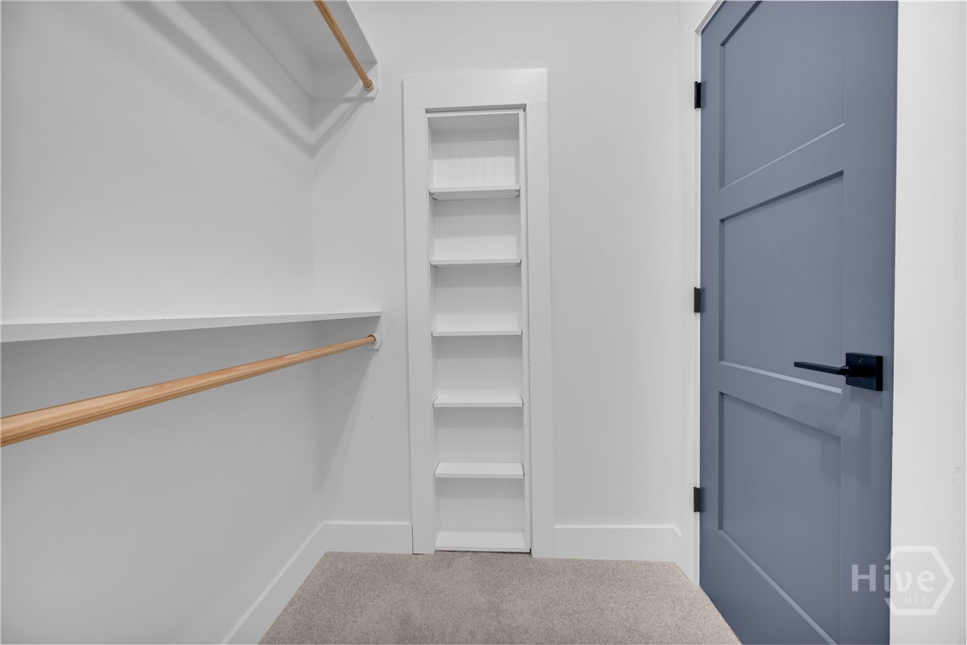 Walk-in closet featuring built-in shelving, two hanging rods, and a plush carpeted floor