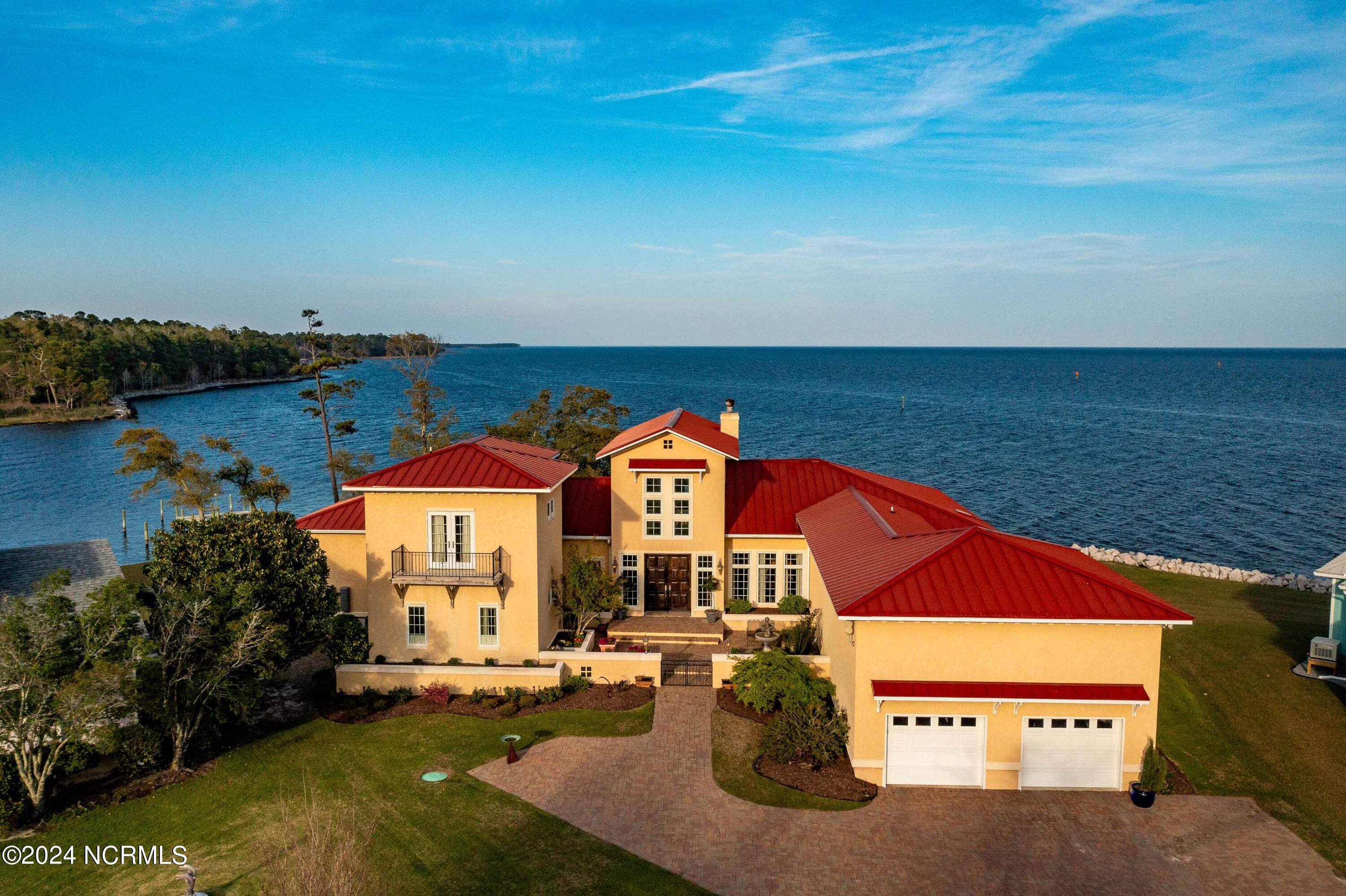6054 Dolphin Road Oriental, North Carolina For those who want it all, this one-of-a-kind property will take your breath away. Situated on an acre of land with over 180-degree views of the Neuse River and the Pamlico Sound, passing sailboats and dolphins bestow a touch of magic. Included is a deeded boat slip with power plus an additional landing/fishing dock. Inspired by the shapes, colors, and serenity of the Tuscany countryside, a master architect designed a contemporary residence with unparalleled views from every room. An embracing courtyard enhanced by a soothing fountain opens to the grand gallery with its soaring vaulted ceiling and the blue views of sky and water beyond. The great room includes a full wet bar with refrigerator and ice, a dining area for ten, and a large conversation area around the fireplace. The bar is just steps from the screened porch and the rear terrace with ample space to entertain. Pass beyond the retaining wall, and enjoy lawn games by the water or just soak in the serenity. The gourmet kitchen features a built in Sub Zero, Viking cooktop, two prep areas, and an adjacent walled courtyard for potted herbs and al fresco dining. A barrel ceiling passage leads to the more private side of the home. A library with built-in bookcases and partner's desk, a guest room with ensuite bath and a private entrance, and the coffered ceiling owner's suite with a private terrace and two bathrooms. His bath has a doorless tile shower and a walk-in closet. Her bath includes a dressing room with built in armoires and a grand soaking tub. Upstairs, a second guest suite includes its own sitting room overlooking the boats leaving Pierce Creek for the big water. The many amenities include sound and security systems, whole house generator, reverse osmosis water, specialty gallery lighting, large laundry/hobby room with drying cabinet and ironing center, irrigation system, pet door, heated bathroom tiles, large walk-up attic, windows with built in shades and pull down screens.
