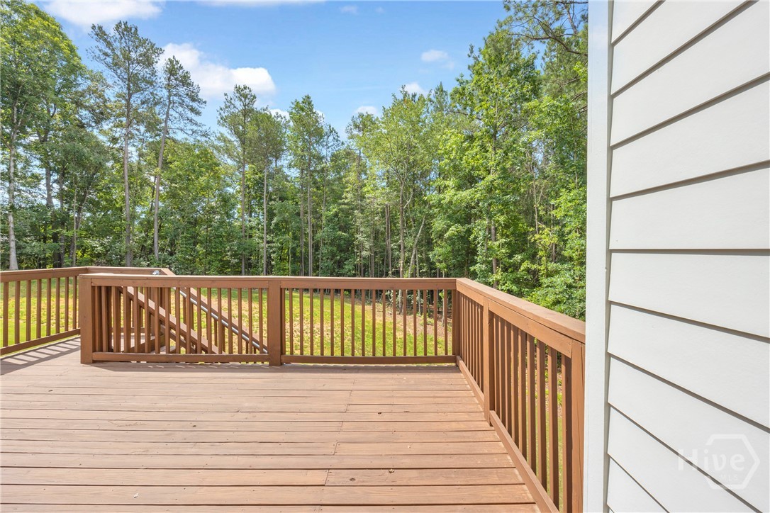 Spacious outdoor deck with wood-finish flooring and railing, featuring stairs descending to a grassy area