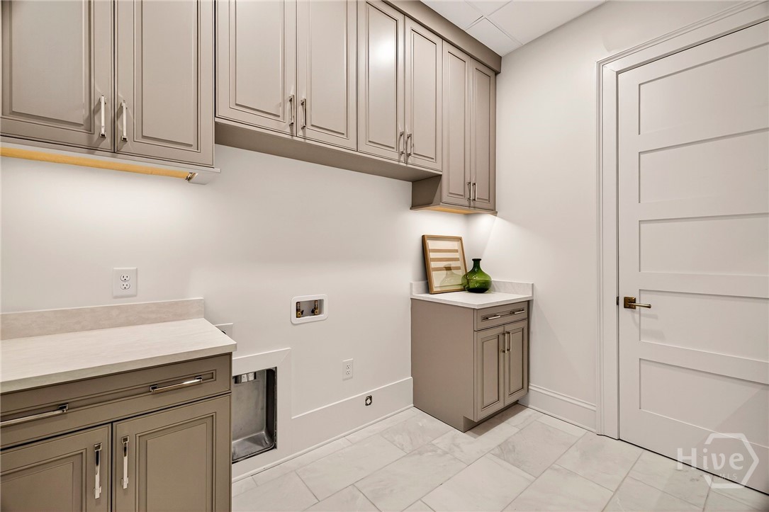 Laundry room - This spacious laundry room features a streamlined layout with upper and lower cabinetry for concealed storage and countertop workspace. Large-format tile flooring and recessed appliance connections ensure functionality, while the neutral palette complements the home’s overall design. A utility zone that blends efficiency with understated elegance.