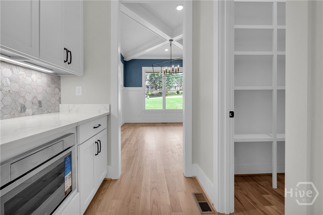 Kitchen featuring bright white cabinetry with black hardware, white countertops, built-in microwave, hexagonal tile backsplash with under-cabinet lighting, and wood-finish flooring