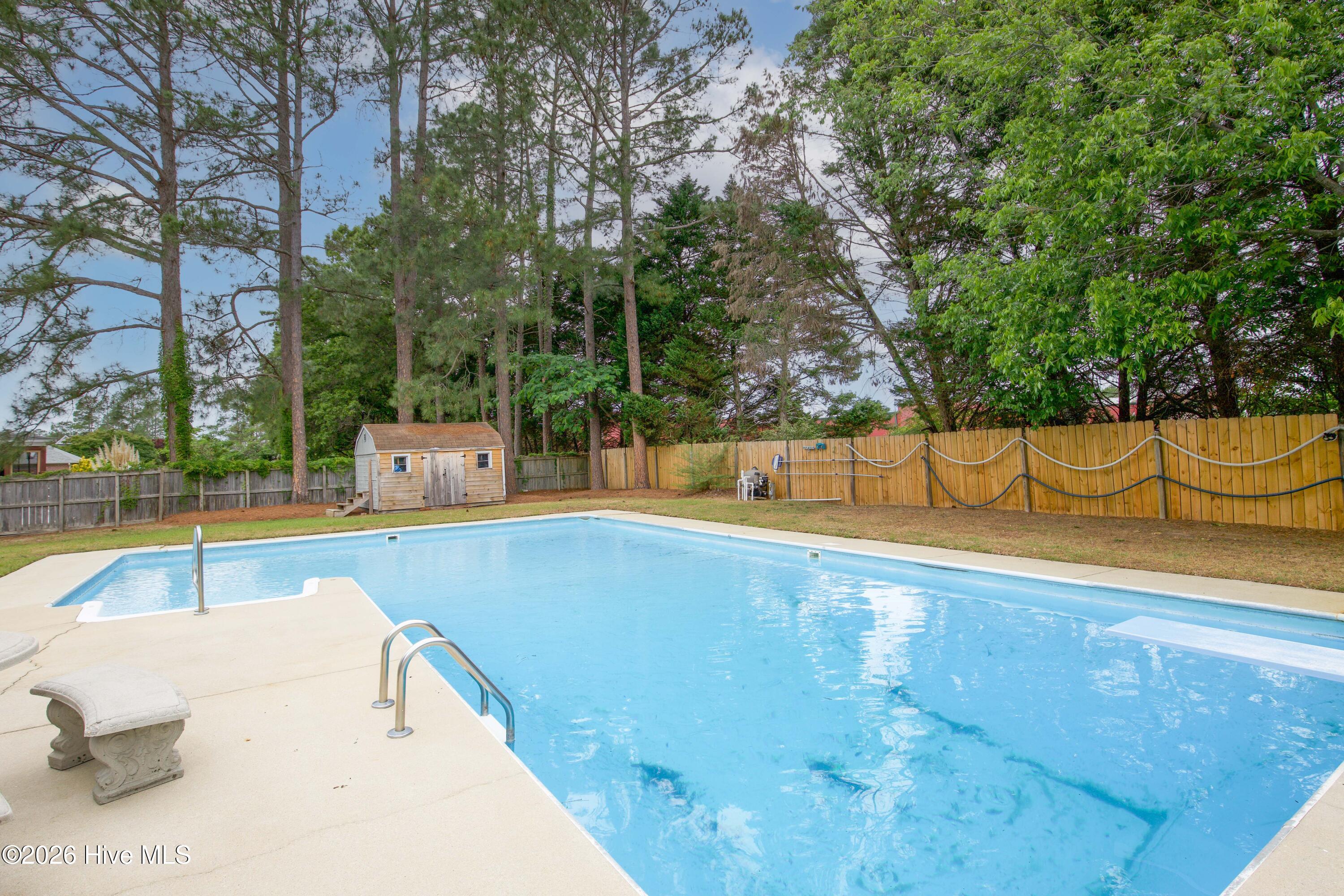 Poolside view capturing the scale, privacy, and functionality of this impressive outdoor entertaining space. The large in-ground pool is surrounded by generous patio areas and mature landscaping, creating a peaceful backyard environment with room for entertaining, outdoor dining, and recreation. Outdoor spaces like this remain highly sought after among military relocation and PCS buyers in the Fayetteville area.