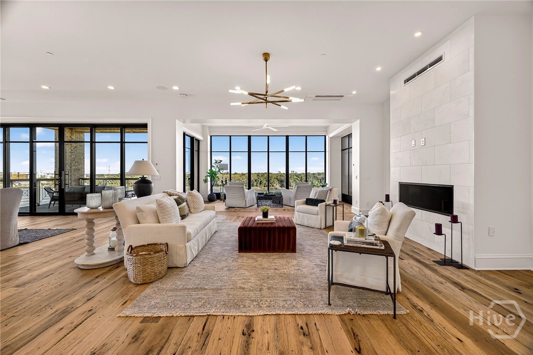 Living room with floor-to-ceiling windows. Expansive living area designed for seamless indoor-outdoor living and elevated entertaining. Floor-to-ceiling windows frame lush views, while dual seating zones and a minimalist fireplace create a warm, open ambiance. The layout invites flexible use while maintaining a luxurious sense of space.