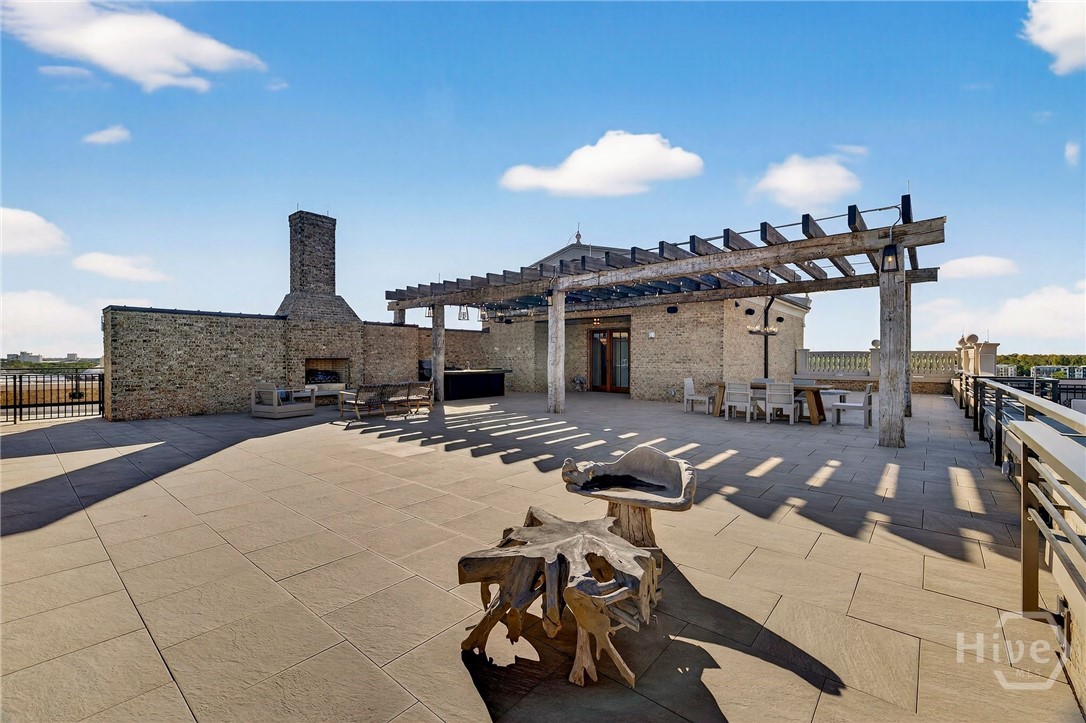A private sculptural rooftop retreat featuring a stone fireplace, pergola shade structure, and open lounge area. Natural materials and layered zones create visual interest and functional versatility. An outdoor living space designed for elevated gatherings and artistic ambiance.