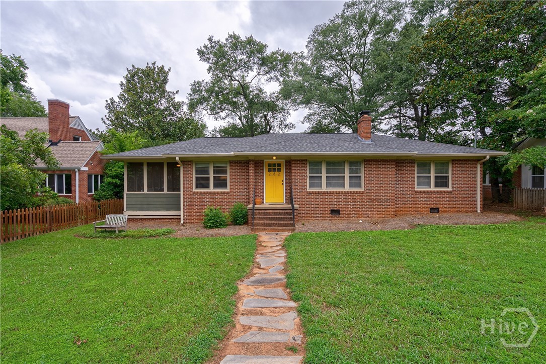 Situated on a rare oversized intown lot with frontage on both Holman Avenue and Best Drive, this updated midcentury brick ranch offers unique possibilities. The front door is located off sidewalk-lined Holman Avenue and the back of the property provides easy access from Best Drive, ideal for a future detached garage with a guest apartment above, a pool house, or additional parking. The large, flat yard is perfect for entertaining, gardening, or even adding a pool. Located in the highly desirable Normaltown neighborhood, you’ll be within walking distance of the new University of Georgia Medical College, Piedmont College, Piedmont Hospital, St. Mary’s Hospital, and the popular farmers market in Bishop Park. You can grab a pizza at Automatic, enjoy a coffee at Sips, or explore the many local shops and restaurants just minutes from your front door.
Great curb appeal greets you with a large grassy front yard, a stone path, and an inviting yellow front door. Inside, the living room features hardwood floors, abundant natural light from triple front windows, and a brick wood-burning fireplace that can be converted to gas logs. The open-concept layout flows into the dining room and renovated kitchen with white cabinets, an oversized island, leathered black granite countertops, white subway tile backsplash, wood vent hood, and gas range; a perfect setup for any home chef who loves to cook and entertain. The spacious screened-in side porch is located off the dining area, perfect for enjoying fall afternoons, and connects directly to the backyard for seamless indoor-outdoor living.
The oversized primary suite offers both a sleeping area and sitting area, hardwood floors, recessed lighting, and a ceiling fan. The renovated primary bath feels like a private spa with a double vanity topped in granite, an expansive tiled walk-in shower with frameless glass door, and abundant storage space; ideal for keeping everything neatly tucked away. Two secondary bedrooms share an updated hall bath with a white vanity, granite countertop, shower/tub combo with tile surround, and charming period tile floors. Hardwood floors extend throughout the home with no carpet anywhere. A large laundry room provides extra storage space, and the backyard’s size and flat layout make it ideal for gatherings, recreation, or future expansion.