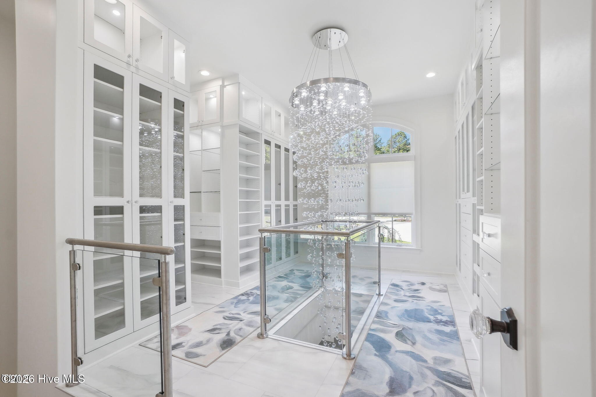 Two story primary closet with custom cabinetry, lighting and two floor chandelier