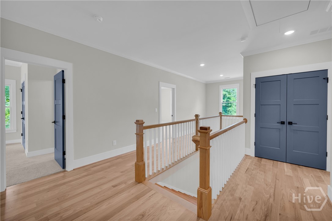 Upper-level hallway featuring wood-finish flooring, white baluster railing with wood newel posts, recessed lighting, and panel doors with dark hardware