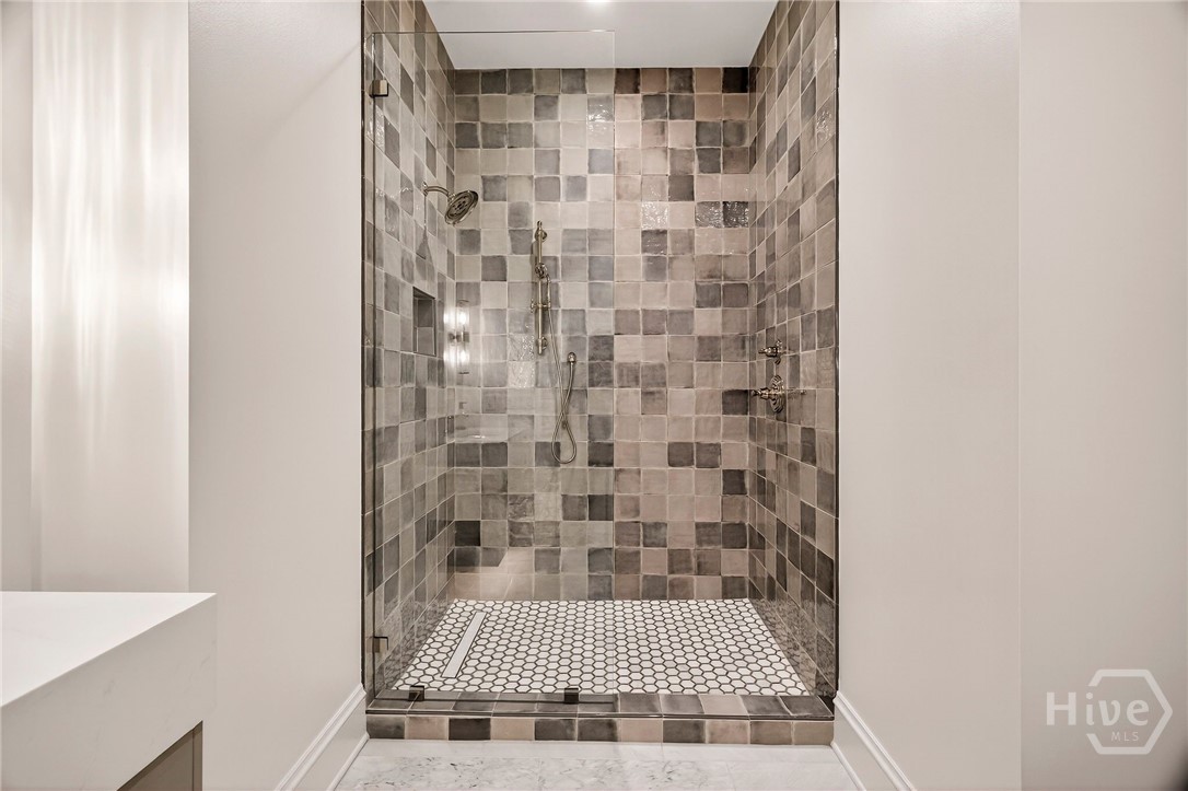 Bedroom 3 Ensuite - This ensuite shower showcases a striking tile composition with layered textures and a symmetrical layout. Dual showerheads and a glass enclosure enhance usability, while marble flooring and recessed lighting complete the elevated experience. A refined bath retreat within the private suite.