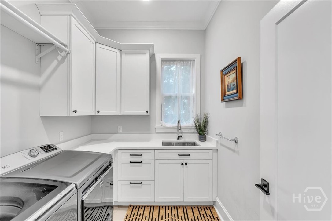 Spacious laundry with sink, hanging rod, and storage cabinetry.