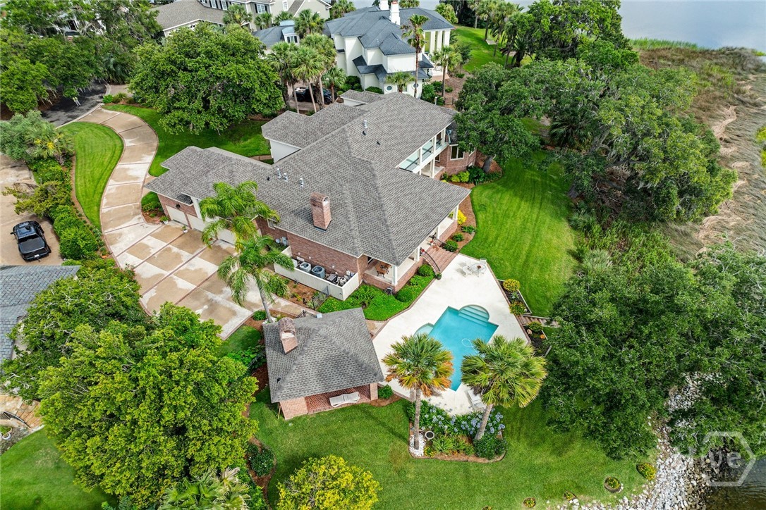 Aerial view of a brick home with a curved driveway, swimming pool, and palm-lined lawn.