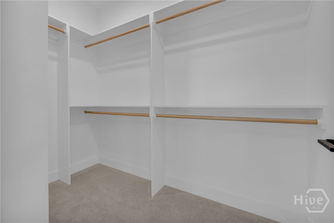 Walk-in closet featuring white built-in shelving, multiple hanging rods, and light gray carpeting