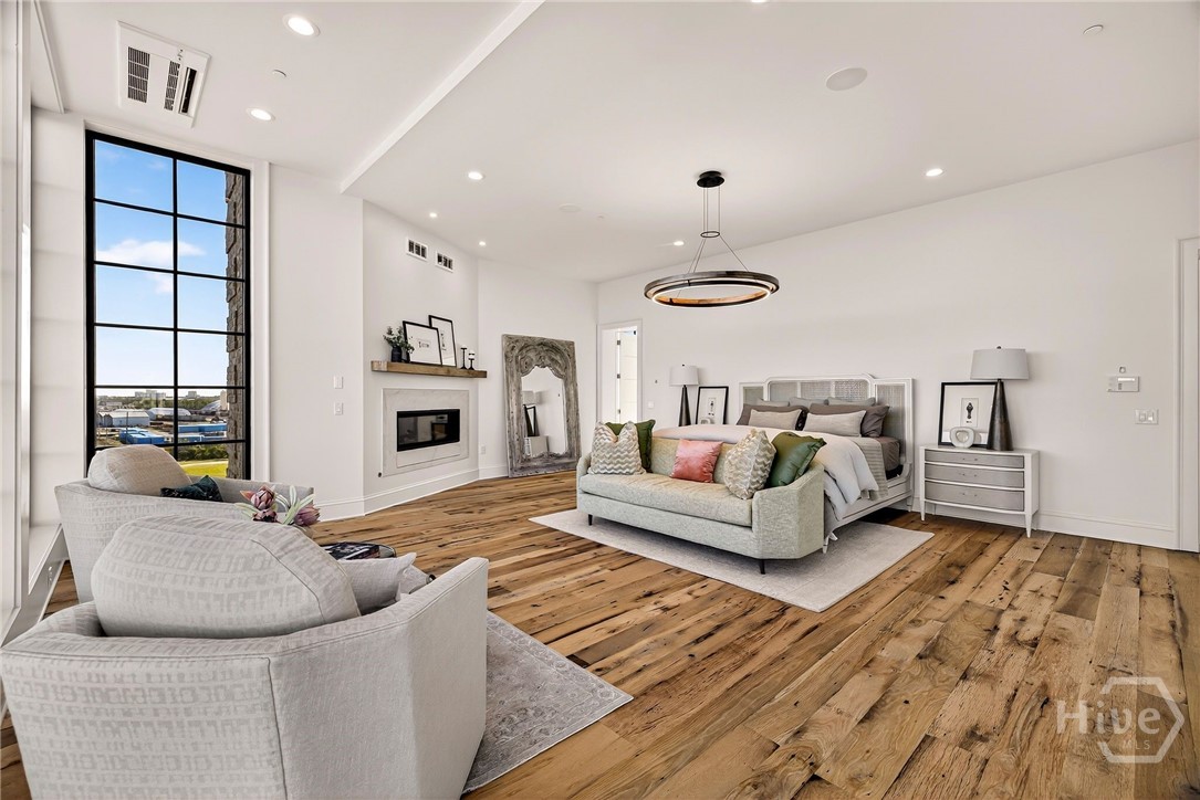 Primary Suite with fireplace and sitting area. This spacious retreat suite is thoughtfully arranged with distinct zones for rest, relaxation, and ambiance. A wall-mounted fireplace and adjacent sitting area enhance the retreat-like feel, while wide-plank flooring and natural light elevate the overall flow. A refined sanctuary with architectural warmth.