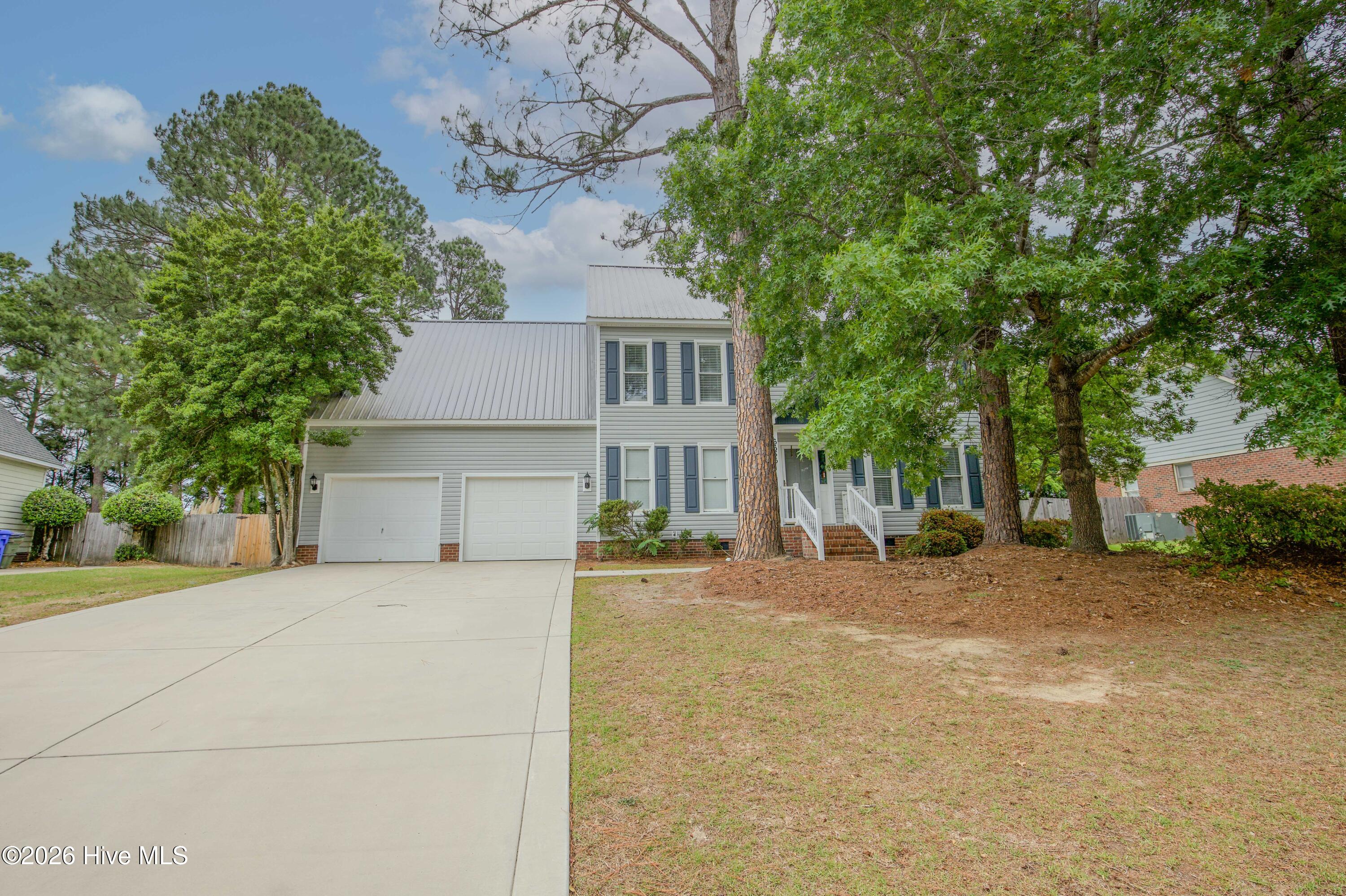 Wide front exterior view showcasing the home’s mature shade trees, oversized driveway, covered front entry, and established curb appeal within the Wells Place community of Fayetteville, NC. Conveniently located near Fort Bragg, Raeford Road shopping, dining, schools, and medical facilities, this spacious two-story property combines functional living with inviting outdoor space and no HOA restrictions.