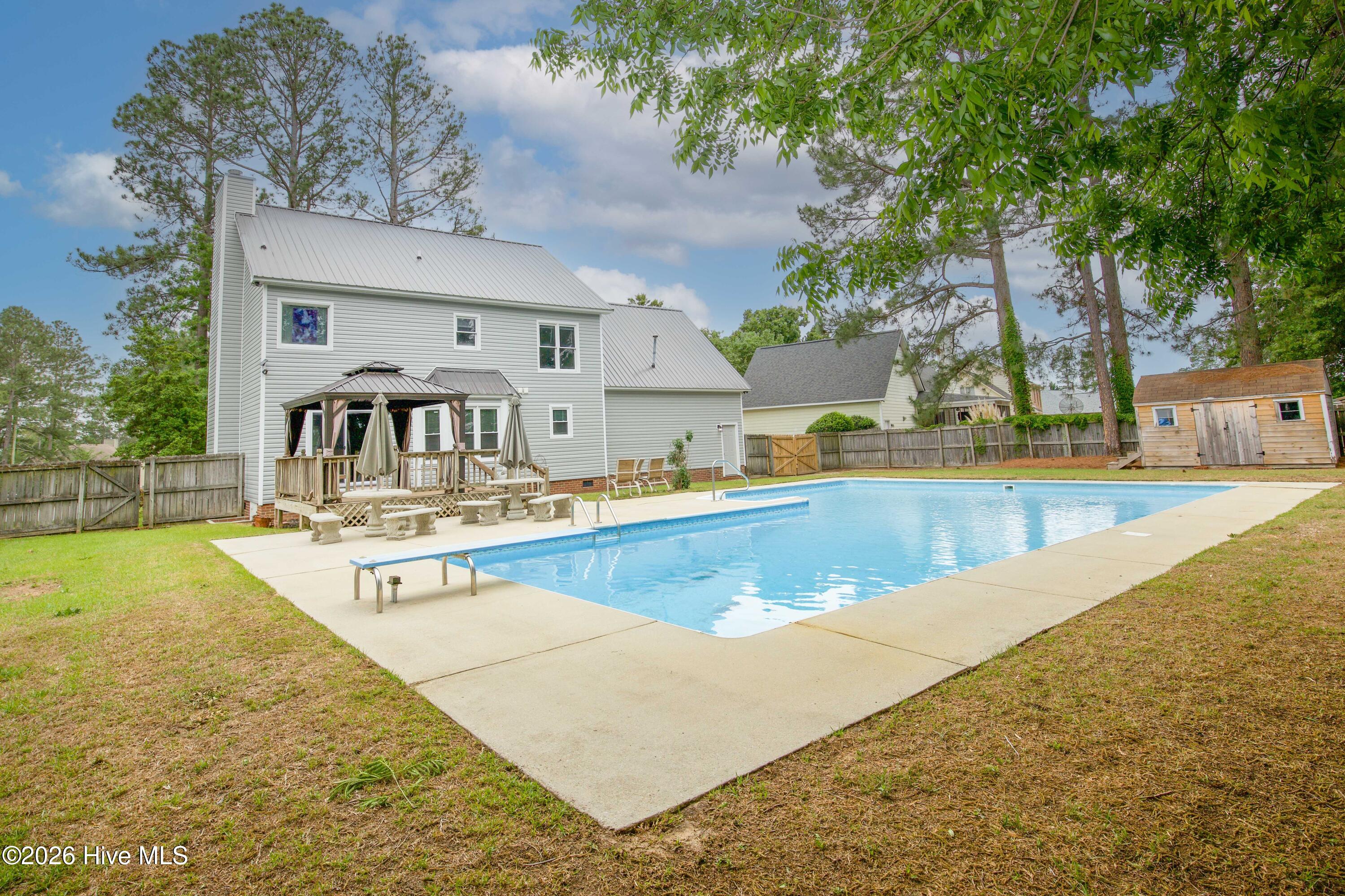 Additional backyard perspective highlighting the relationship between the pool, patio areas, gazebo, and rear exterior of the home. The layout was designed to maximize outdoor enjoyment with multiple gathering areas for entertaining guests, relaxing poolside, or spending time outdoors with family and friends. Large fenced yards with pools and no HOA restrictions remain highly desirable in today’s Fayetteville market.