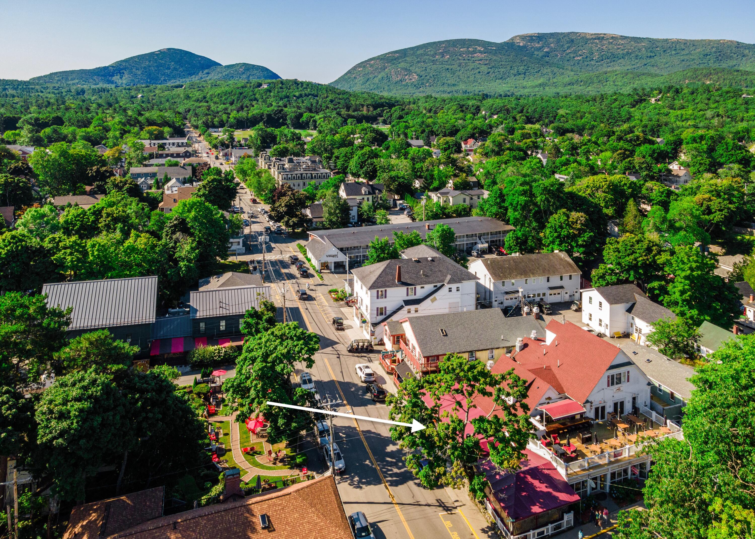 Aerial view of a forested town’s main street, with mountains behind and an arrow pointing to a red-roofed building.