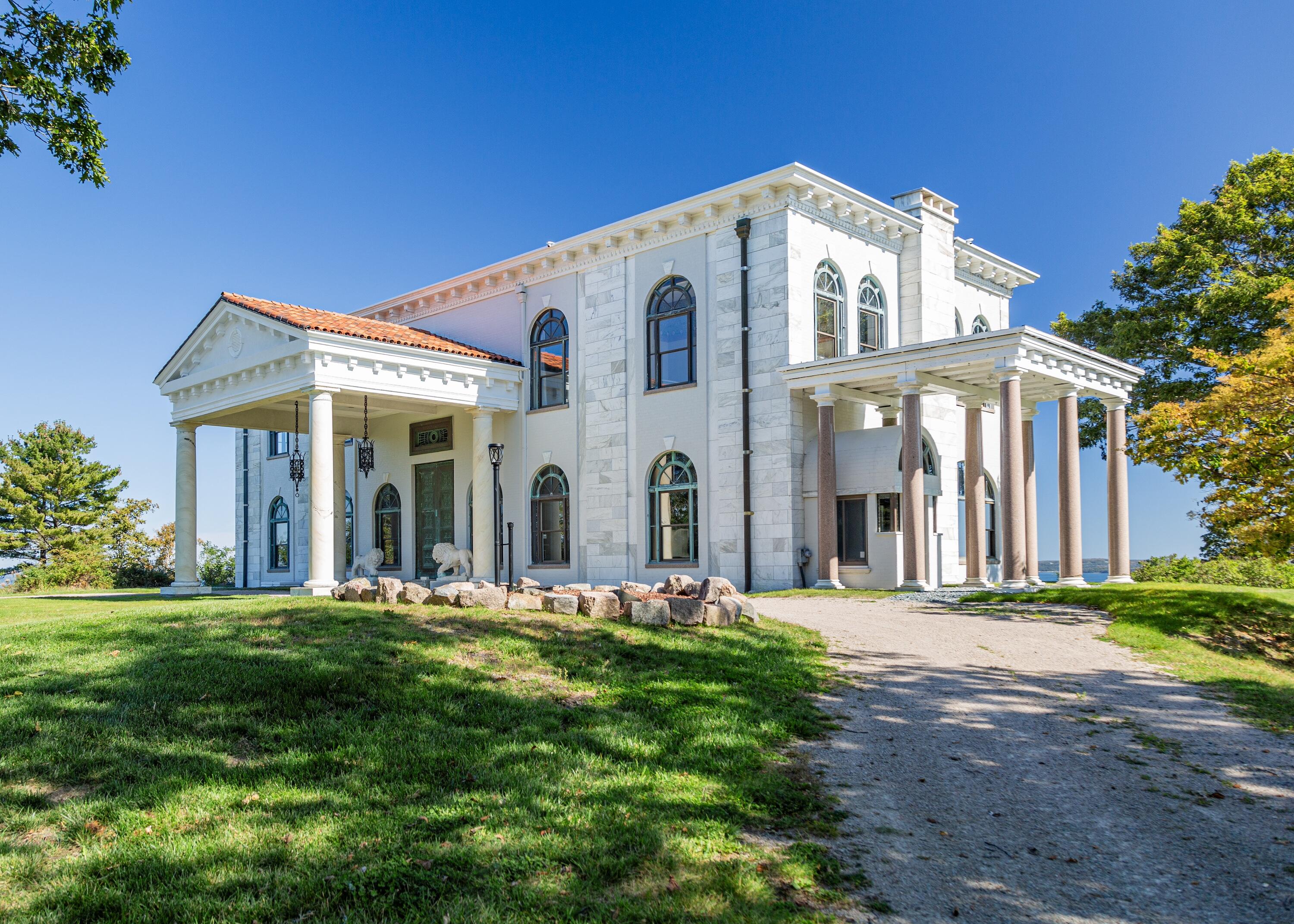 White stone mansion with arched windows and columned porticos beside the water.